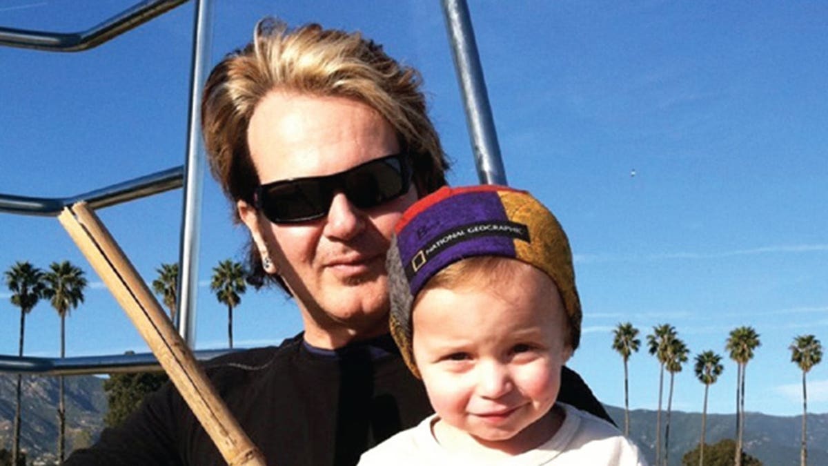 Rikki Rockett holding his son as they play baseball.