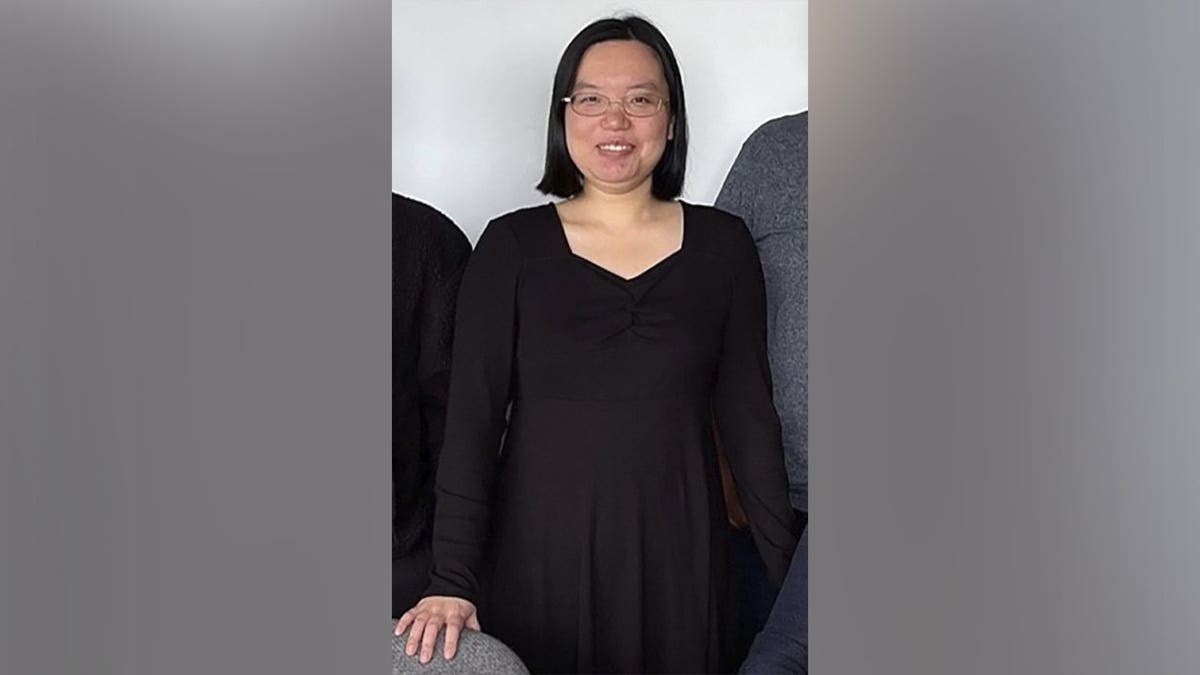 Aili Wang, a University of Wyoming graduate student accused of poisoning a fellow student, stands indoors wearing glasses and a black dress.