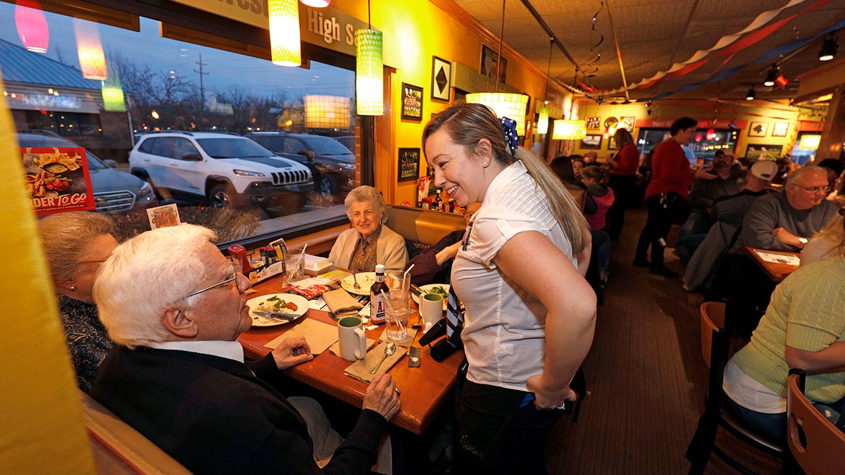 Elderly customers at an Applebee's speak to a smiling waitress.