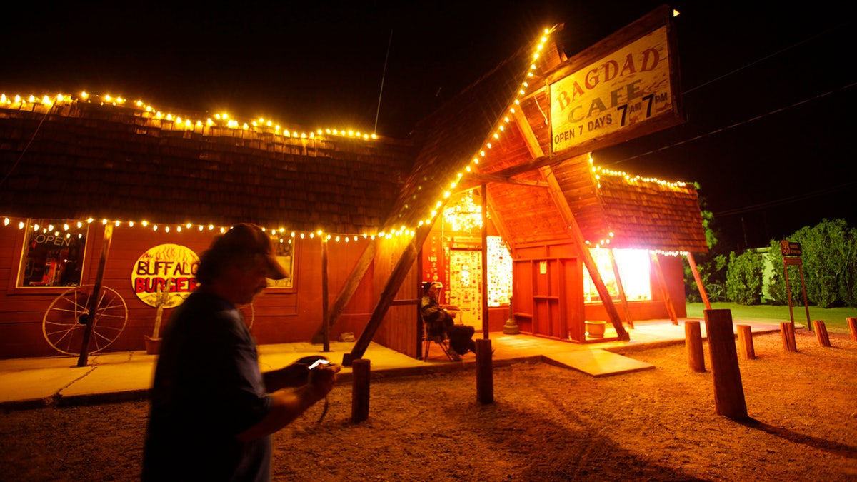 Bagdad Cafe lit up at night as visitor walks by.