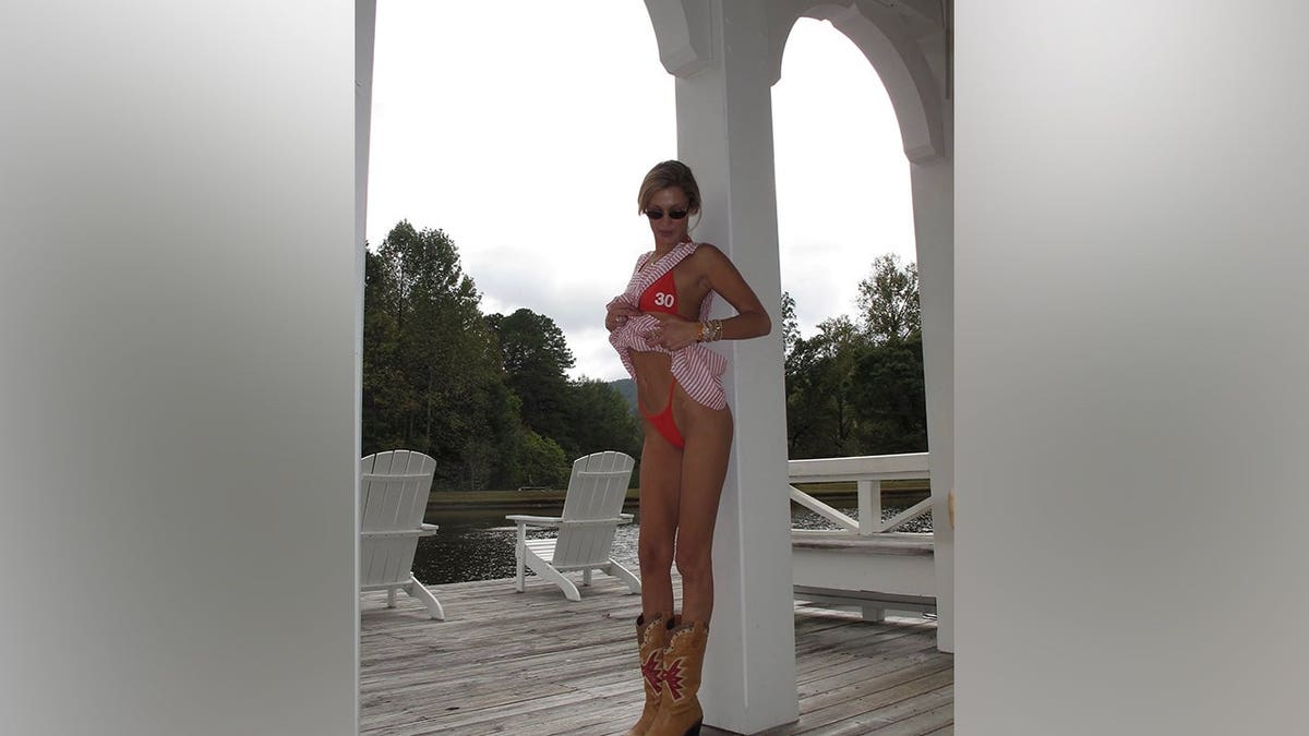 Bella Hadid lifts a pink-and-white striped cover-up while posing in a red bikini and cowboy boots beside a white pavilion.