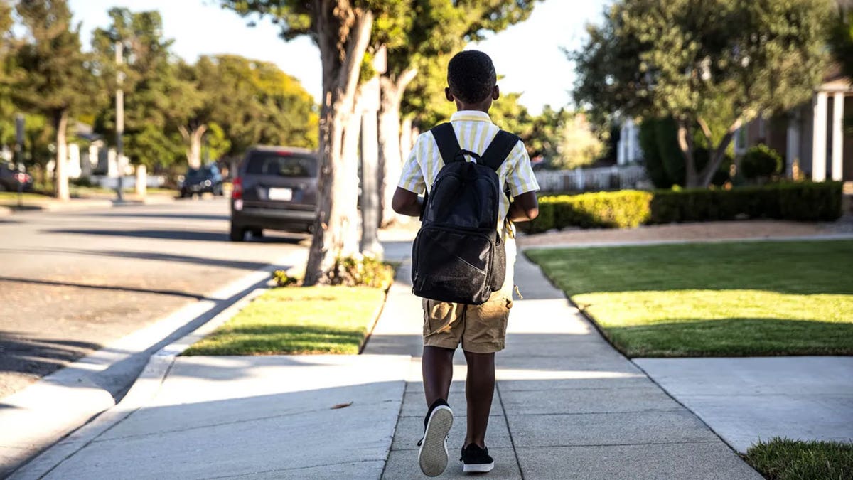 A young boy wearing a backpack walks to school.