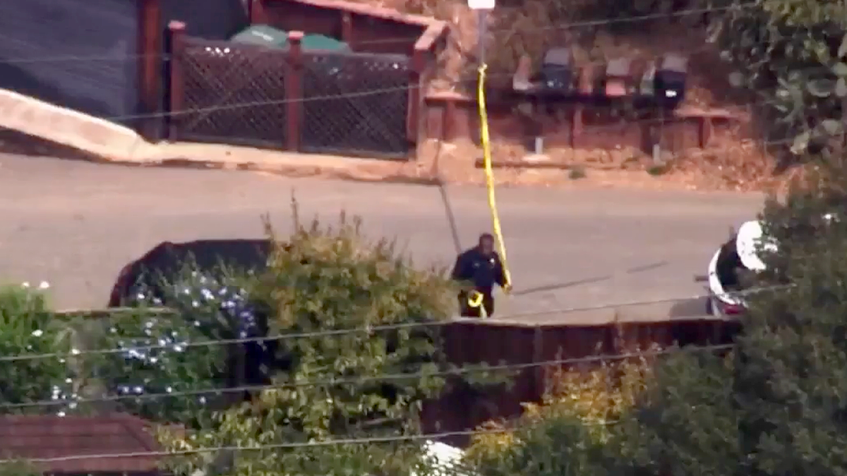 A police officer holding yellow tape near parked vehicles on Panoramic Way