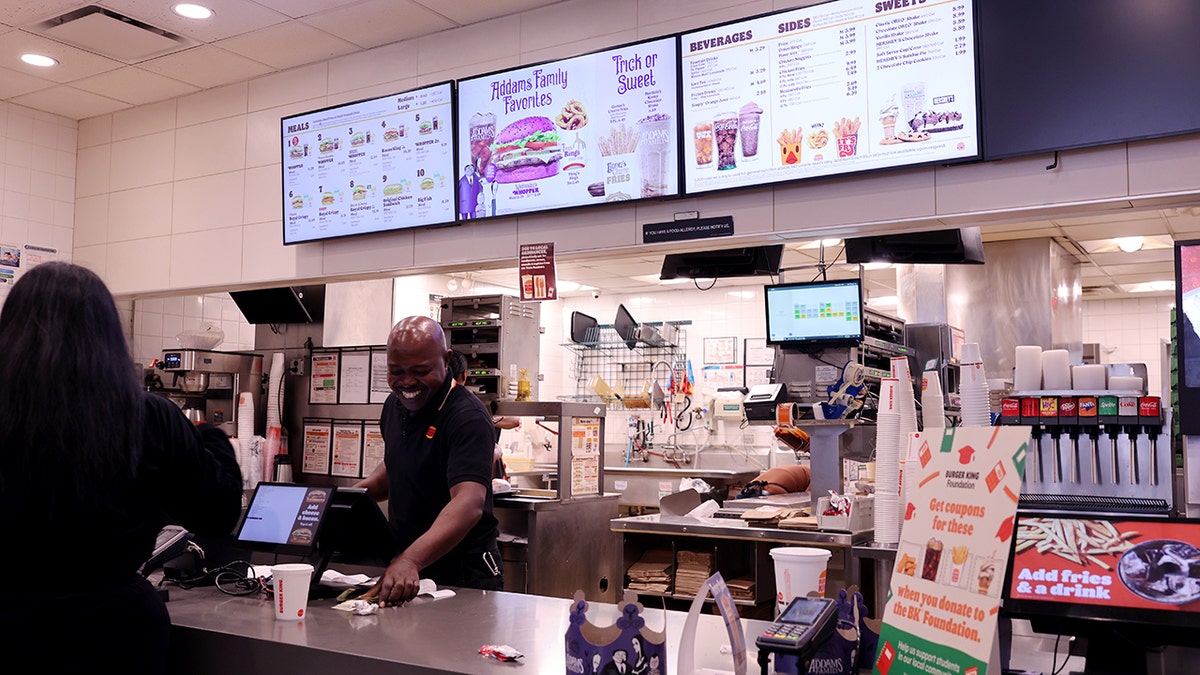 A Burger King employee smiles while tending to a customer at the counter.