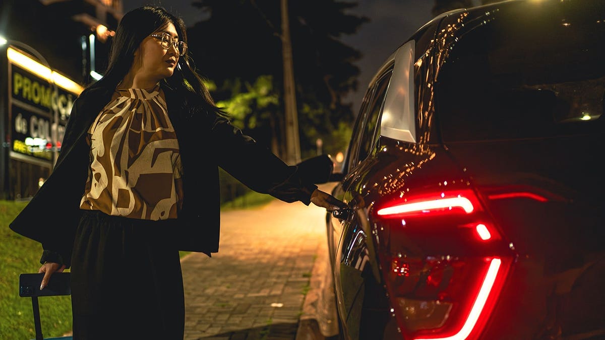 Businesswoman standing beside a rideshare vehicle at night in a city.