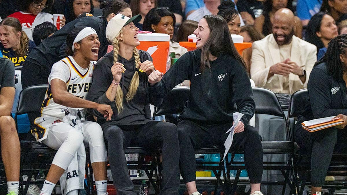 Caitlin Clark laughs on the bench with Sophie Cunningham and Sydney Colson during a game.