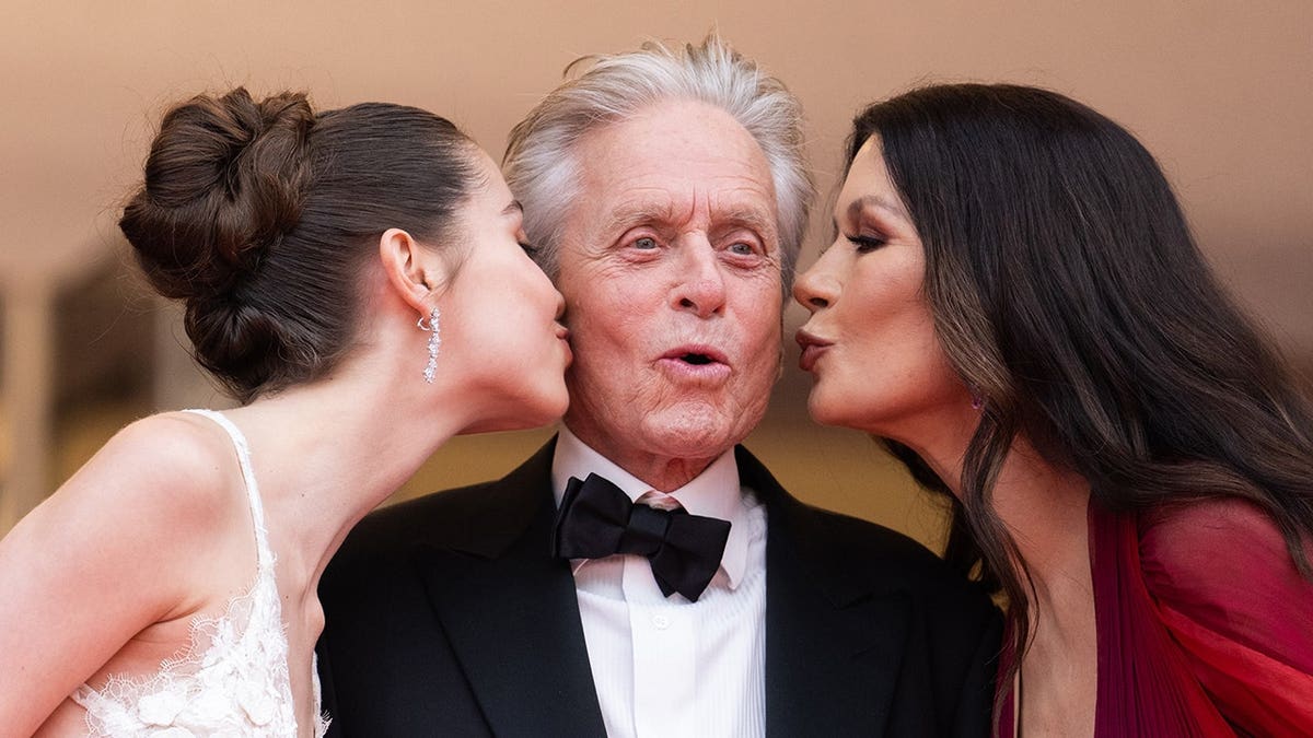 Carys Zeta Douglas, Michael Douglas and Catherine Zeta-Jones stand on a red carpet at Cannes Film Festival.