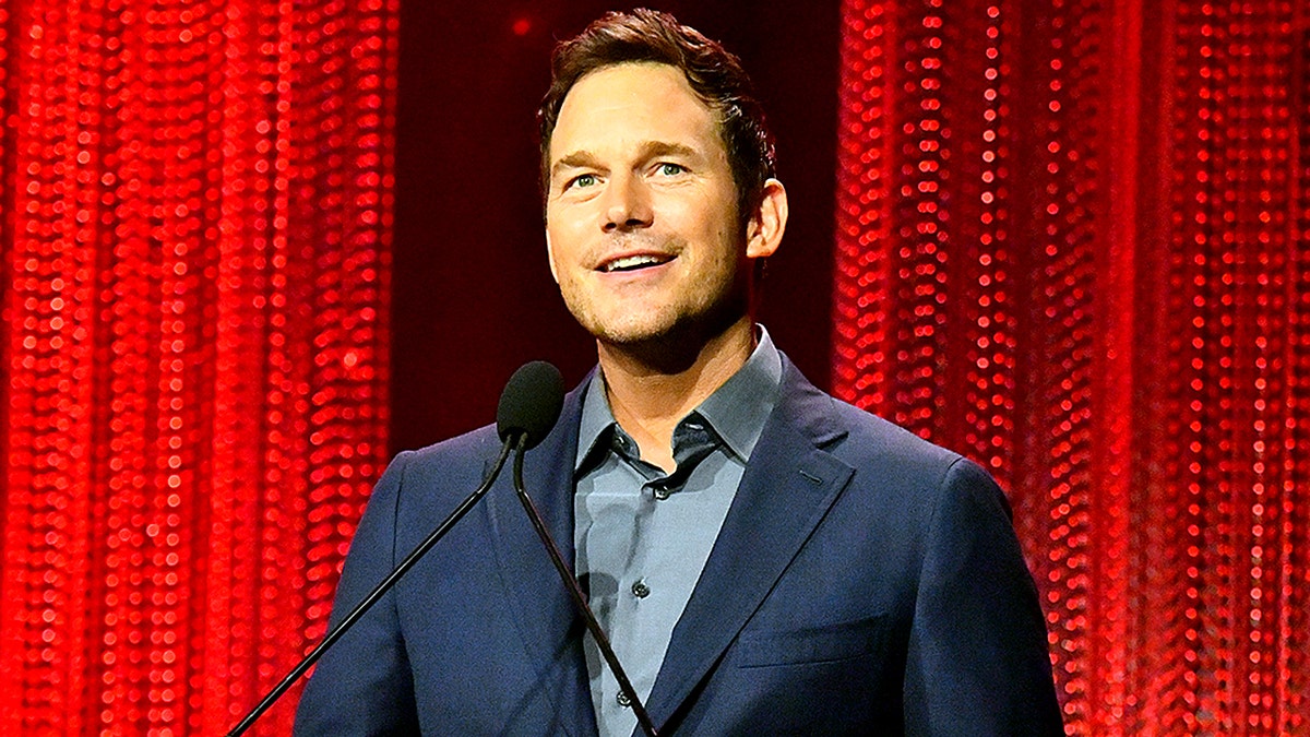 Chris Pratt smiles as he stands at a podium