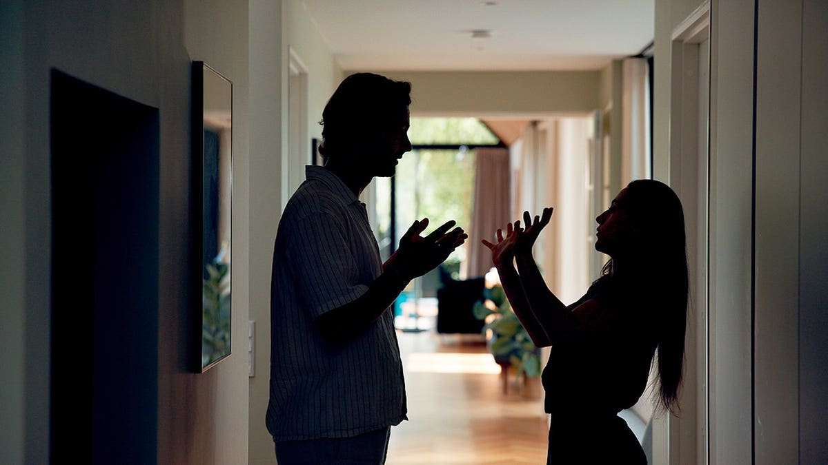 Silhouetted couple stands in hallway during argument
