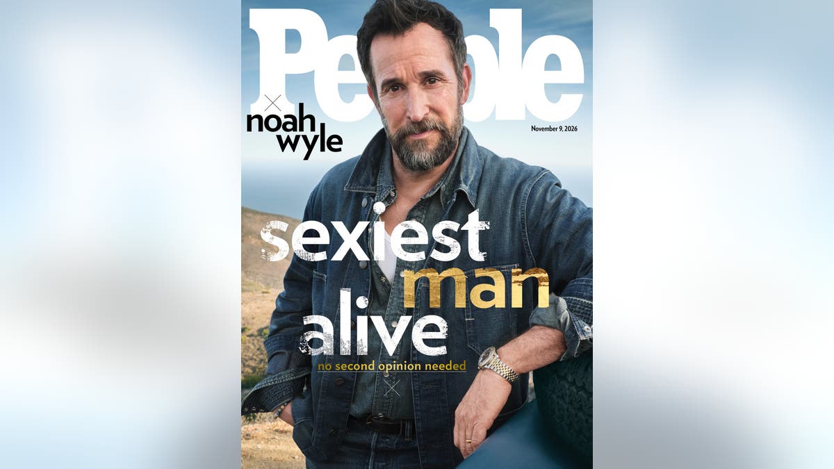 Noah Wyle poses in layered denim clothing with one arm resting on a vehicle tire on a People magazine cover.