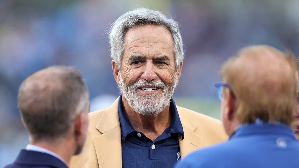 Dan Fouts stands on the field at Tom Benson Hall of Fame Stadium.