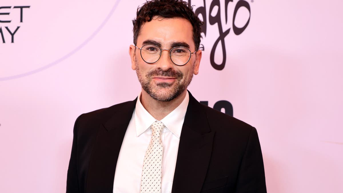 Dan Levy stands at an event backdrop in Los Angeles.