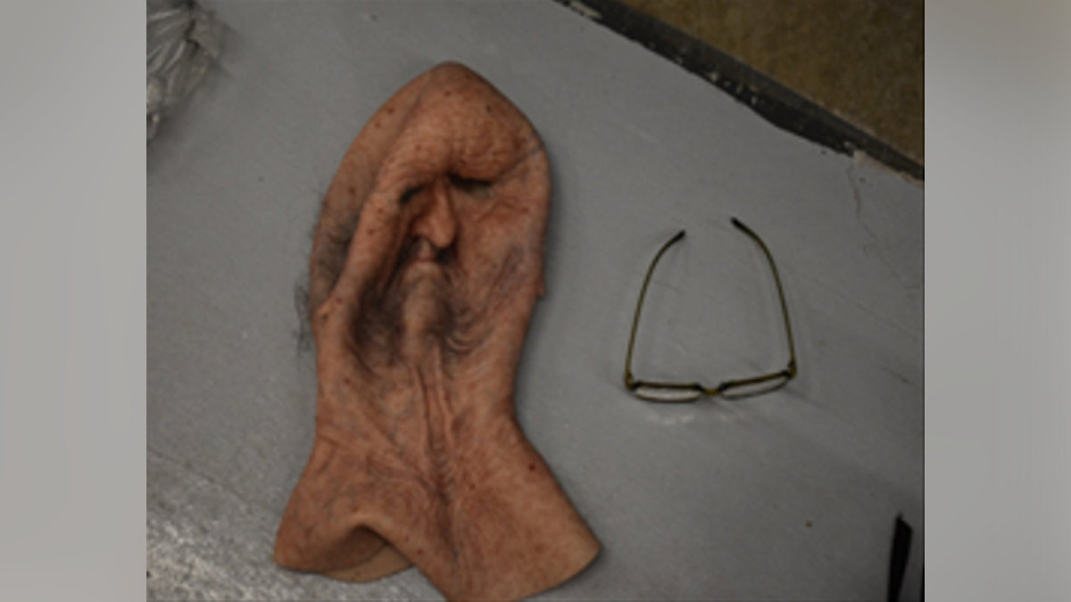 An old man mask and glasses lie on a surface in an evidence photograph