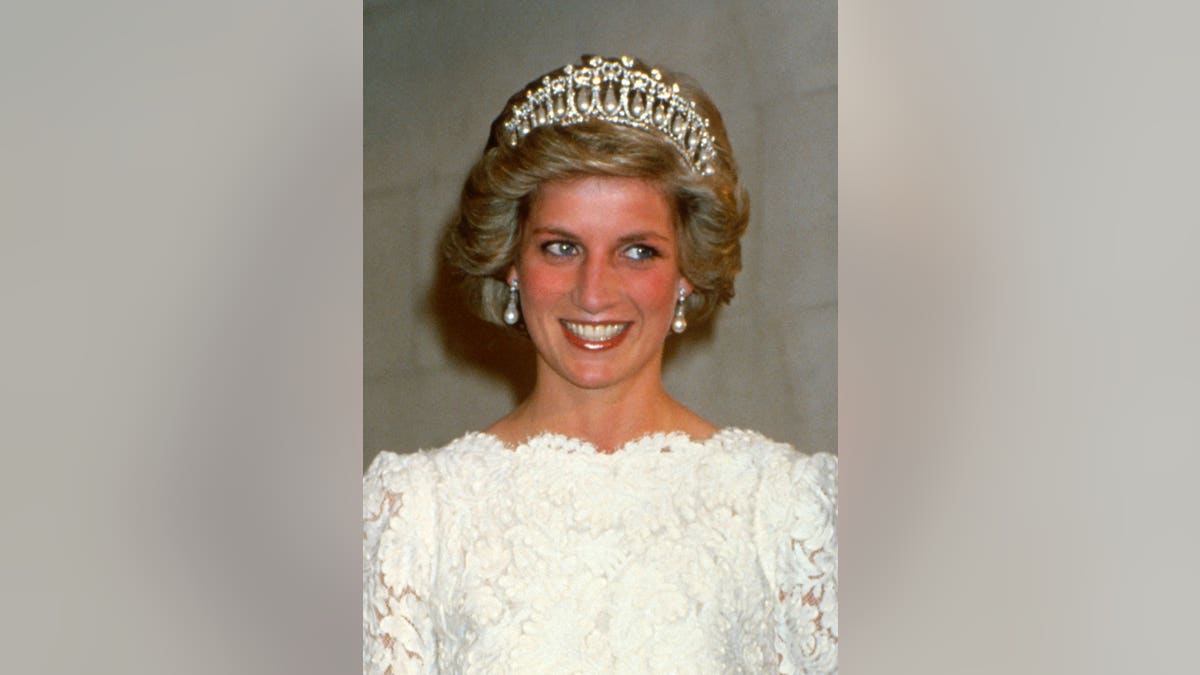 Diana, Princess of Wales, smiles in a cream lace gown and Cambridge Lover's Knot tiara at a dinner.