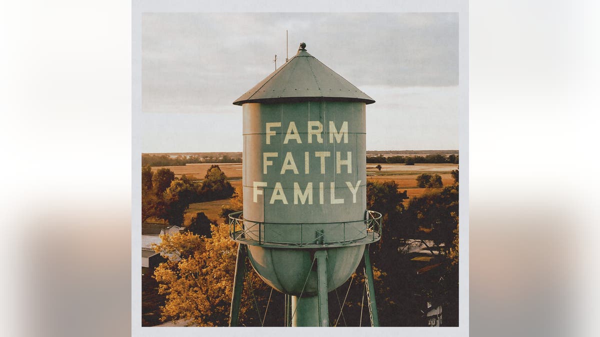 A green water tower displaying the words "Farm Faith Family" stands above trees and agricultural fields.