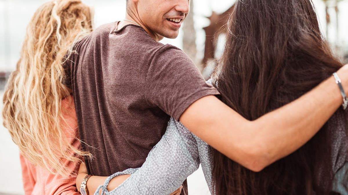 Stock image of a man with his arms around two women.