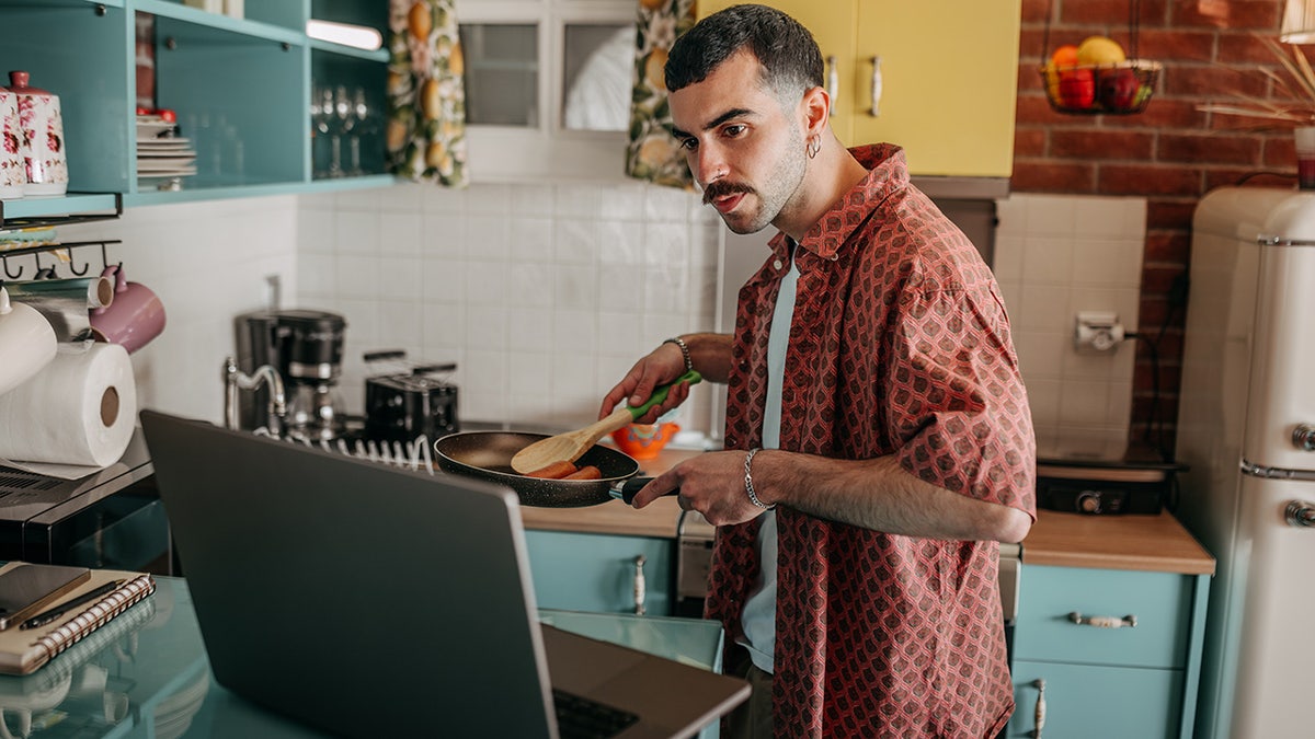 Young casually clothed man having video call while preparing breakfast in a domestic kitchen