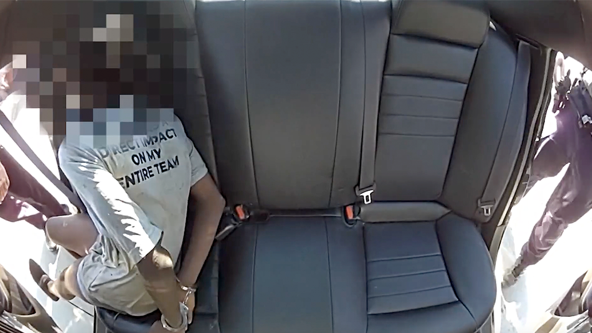 Teenager with a blurred face sits handcuffed in the back of a patrol vehicle