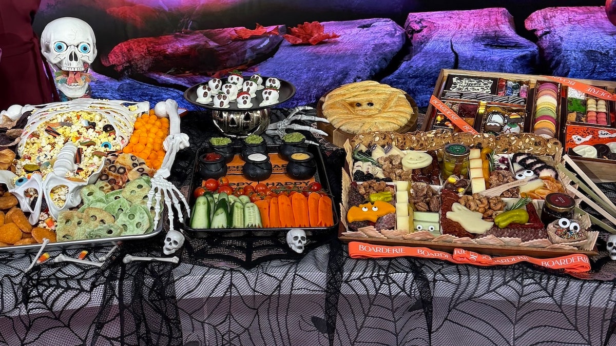 Halloween tablescape with a cheese board, chocolate-covered strawberries and a skeleton snack plate.