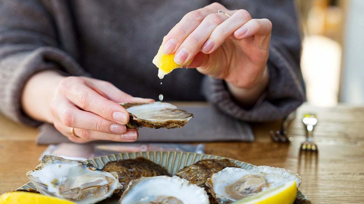 A woman's hand holds a lemon in one hand and an oyster in another.