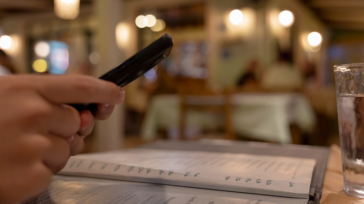 A person's hands holding a cellphone at a restaurant.
