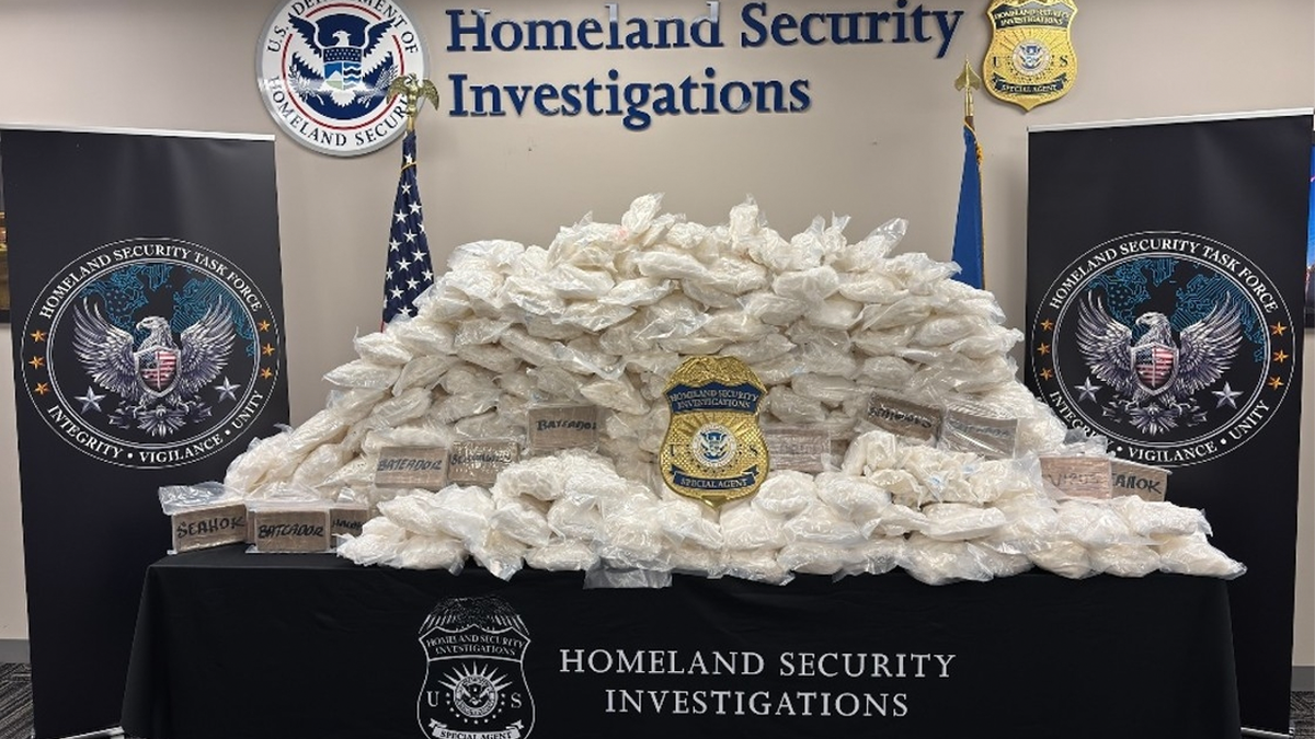 Packaged drugs displayed on a table beneath Homeland Security Investigations signage