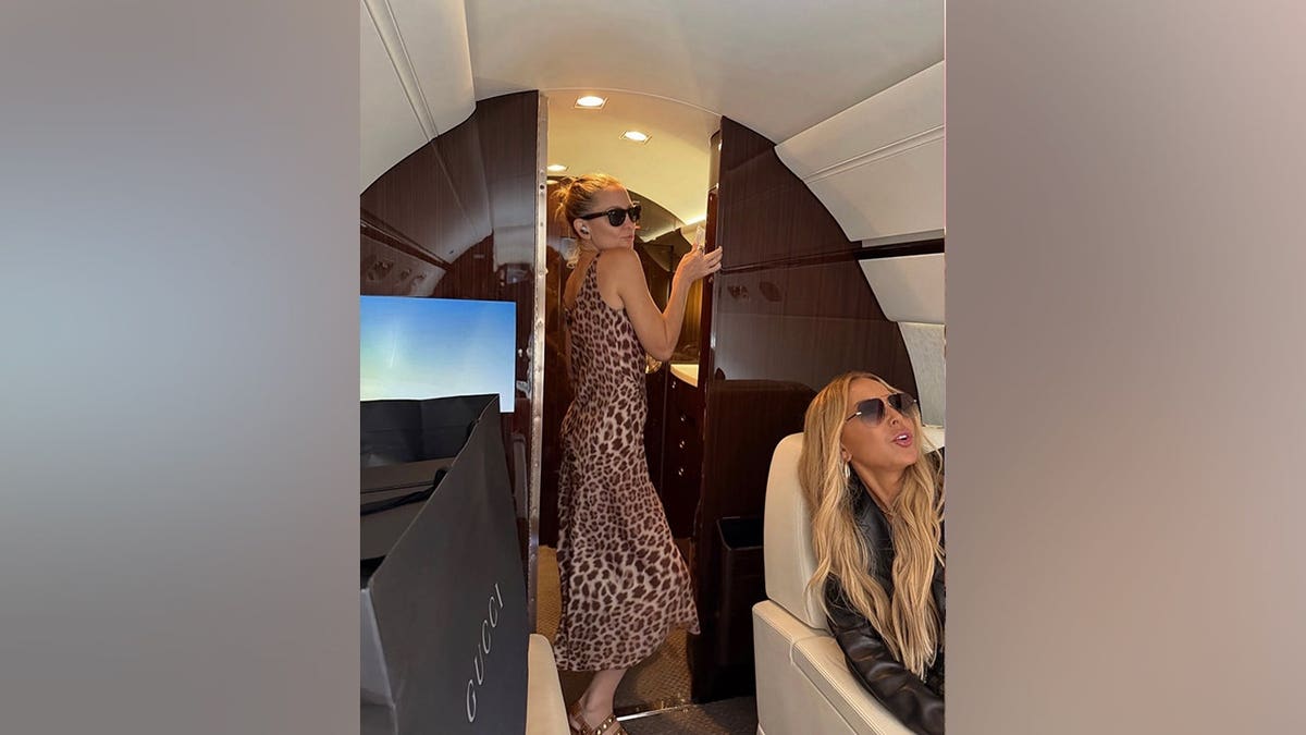 Kate Hudson wears a leopard-print dress and sunglasses while posing aboard a private jet with a friend seated nearby.