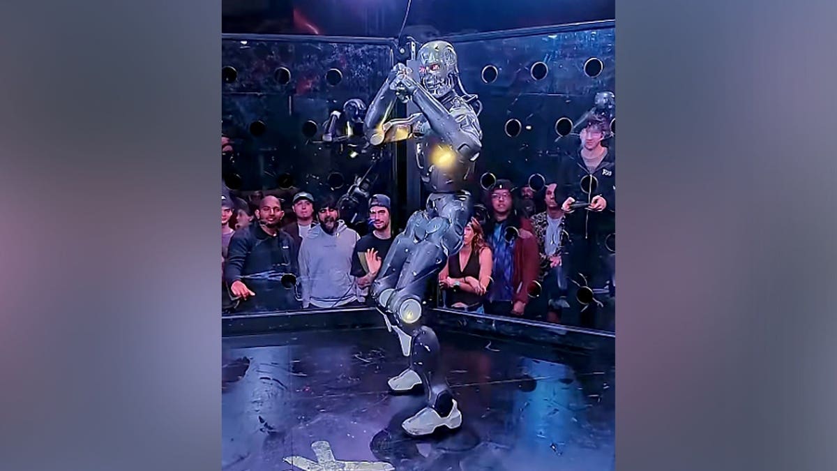 A humanoid robot stands inside a cage, prepared to fight.