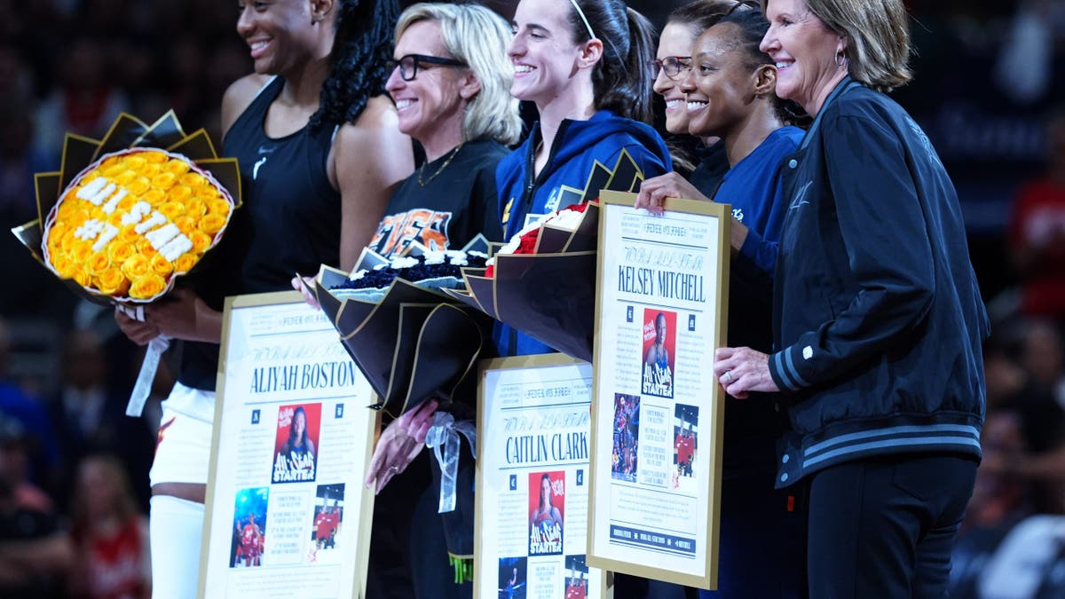 Aliyah Boston, Caitlin Clark, Kelsey Mitchell and Indiana Fever team officials pose at center court.
