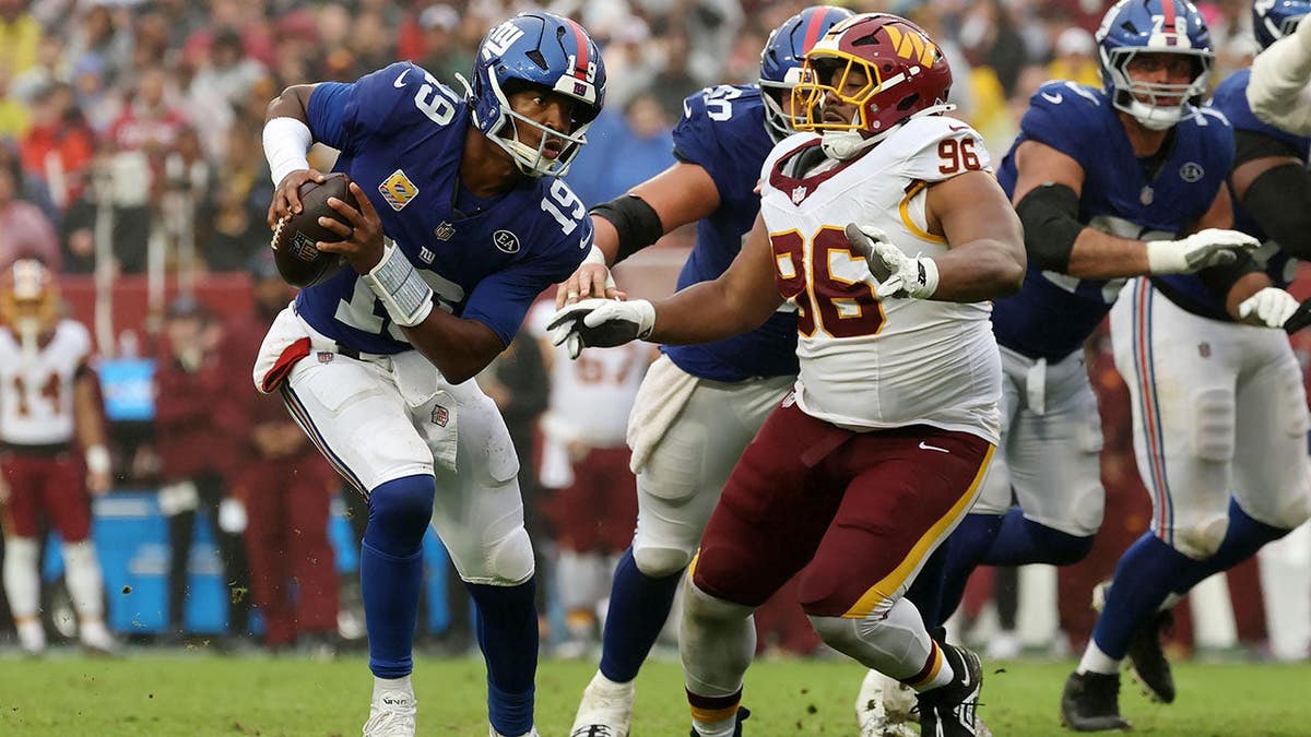 Jameis Winston of the New York Giants looks to pass under pressure from Shy Tuttle of the Washington Commanders.