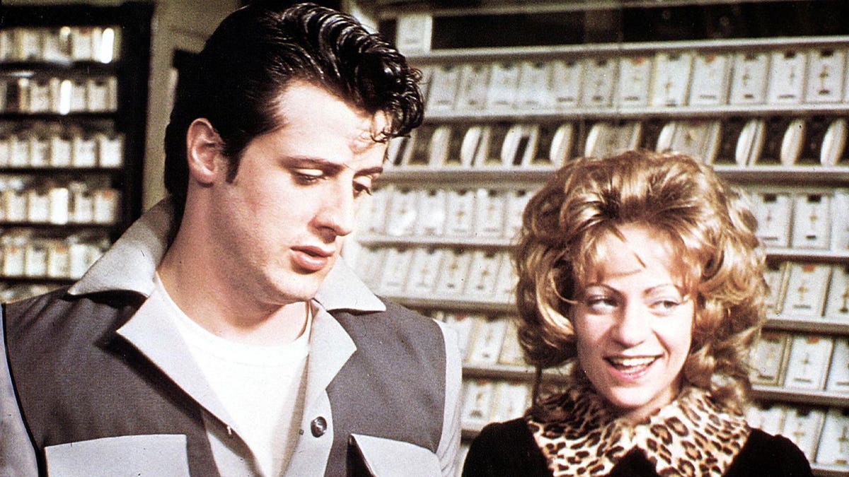 Sylvester Stallone stands with a woman in a jewelry store scene from a film.
