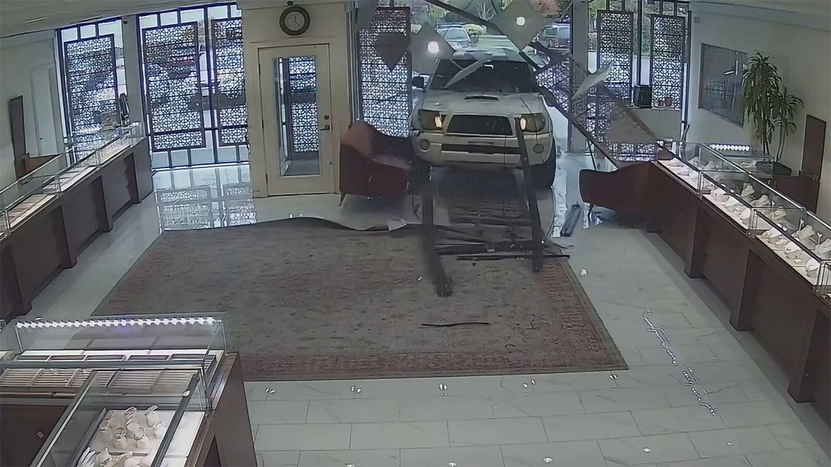 White Toyota Tacoma crashes through storefront as employees run.