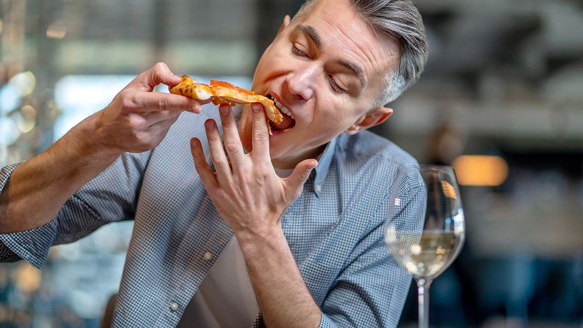 A man eats pizza and appears to enjoy it inside a pizzeria.