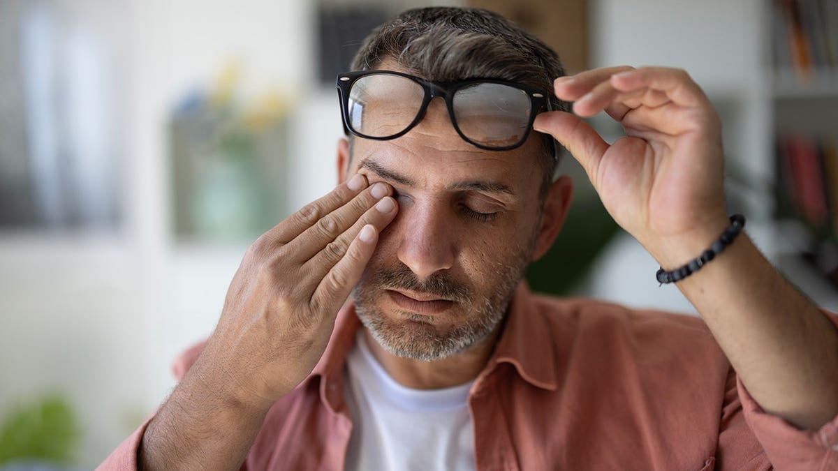 Man rubs his eyes and removes his glasses while experiencing eye strain.