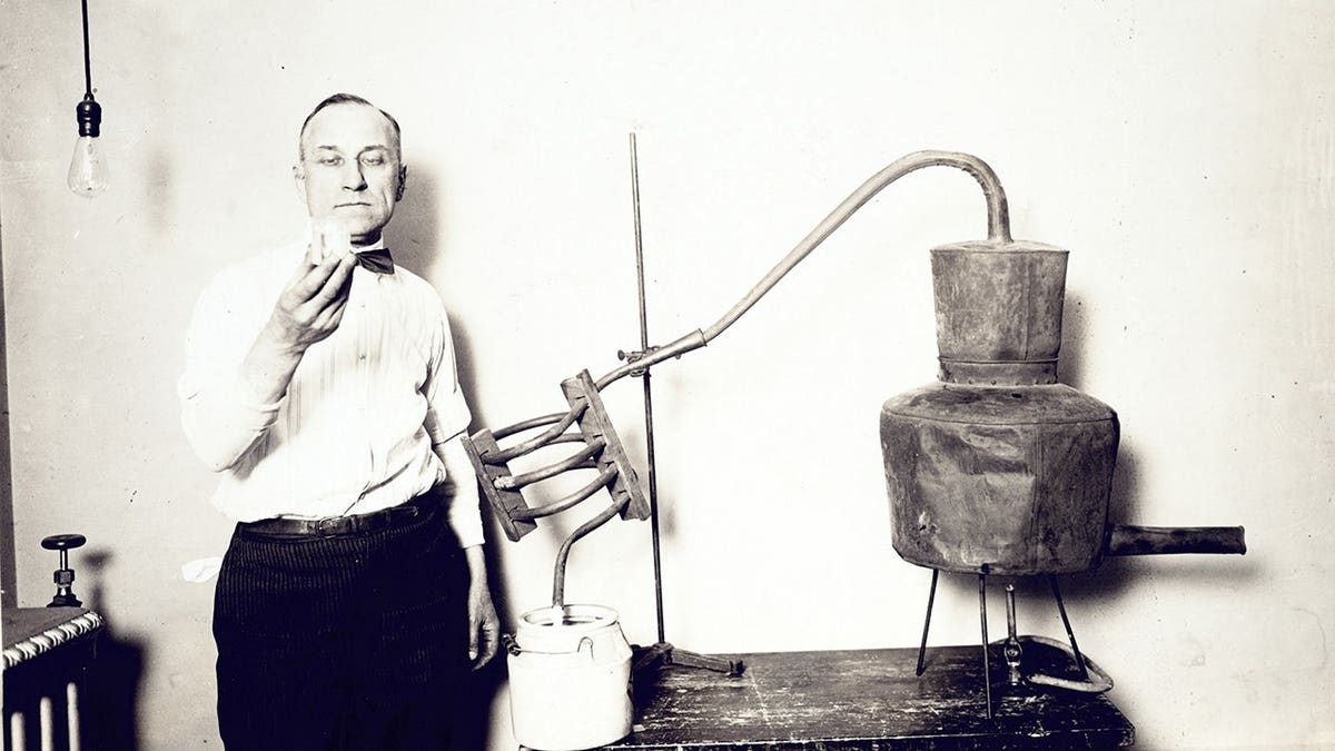Man stands next to a confiscated moonshine still and looks at glass contents.