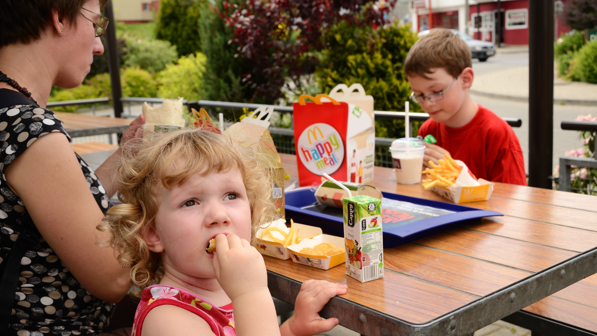 Mother with two children eating lunch at an outdoor McDonald's table in Krakow, Poland.