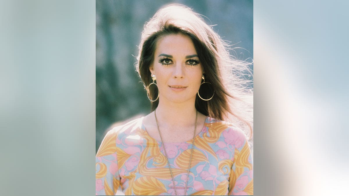 Natalie Wood wears a patterned top with large gold necklace and hoop earrings.