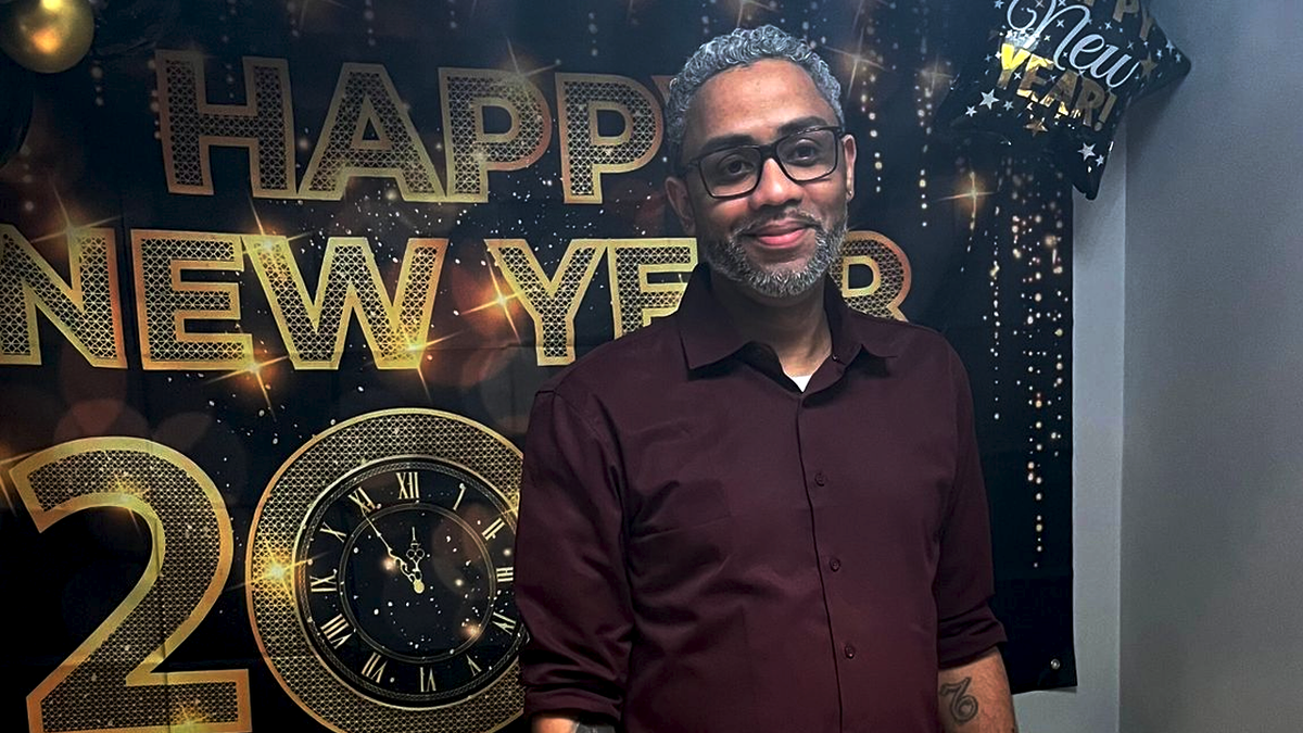 Nelson Batista wearing a maroon shirt in front of a happy new year banner