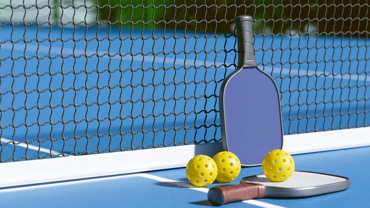 Pickleball paddle and balls rest by the net on a blue court.