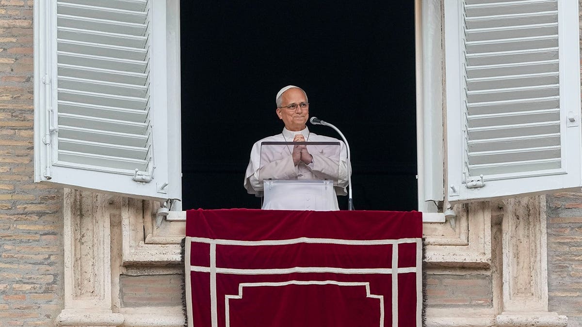 Pope Leo XIV stands at a window in the Apostolic Palace overlooking St. Peter's Square.