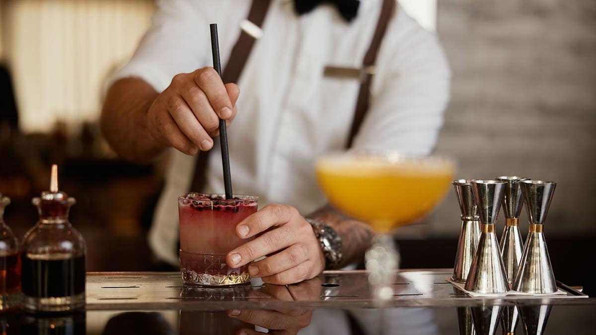 Professional bartender stirs a berry cocktail with a straw at a luxury hotel bar.