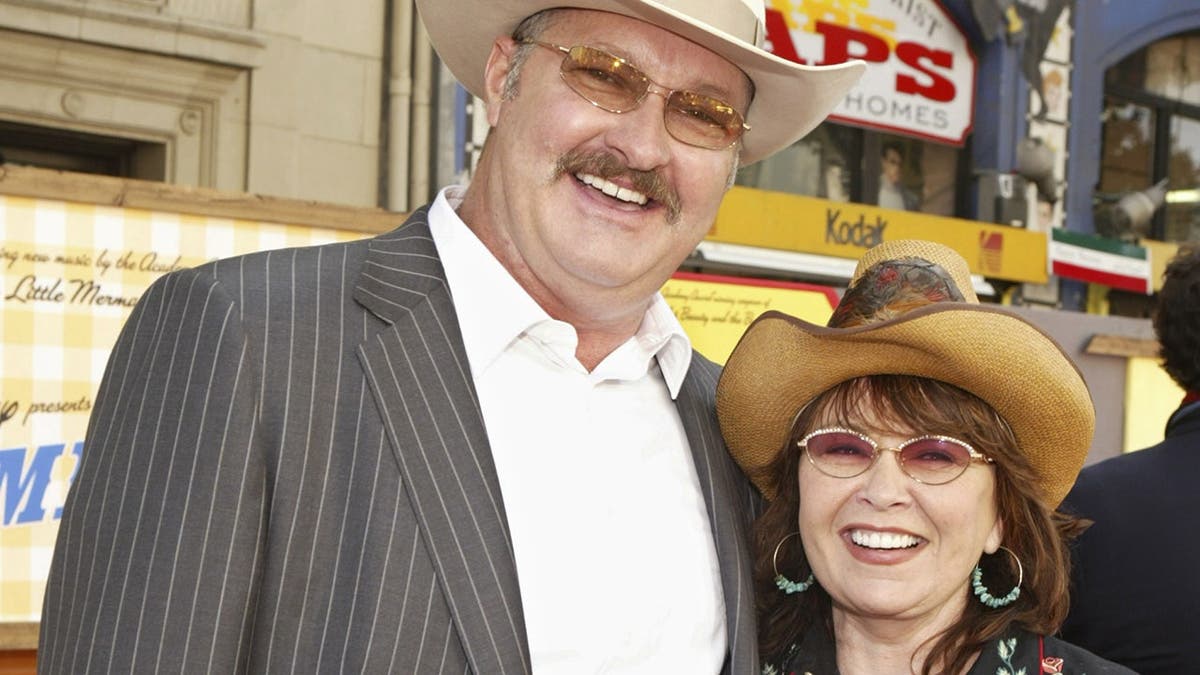 Randy Quaid and Roseanne Barr stand on a red carpet at a premiere.