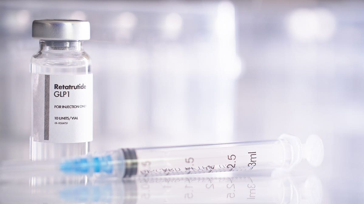 A vaccine vial and syringe containing GLP-1 peptide retatrutide on a surface.