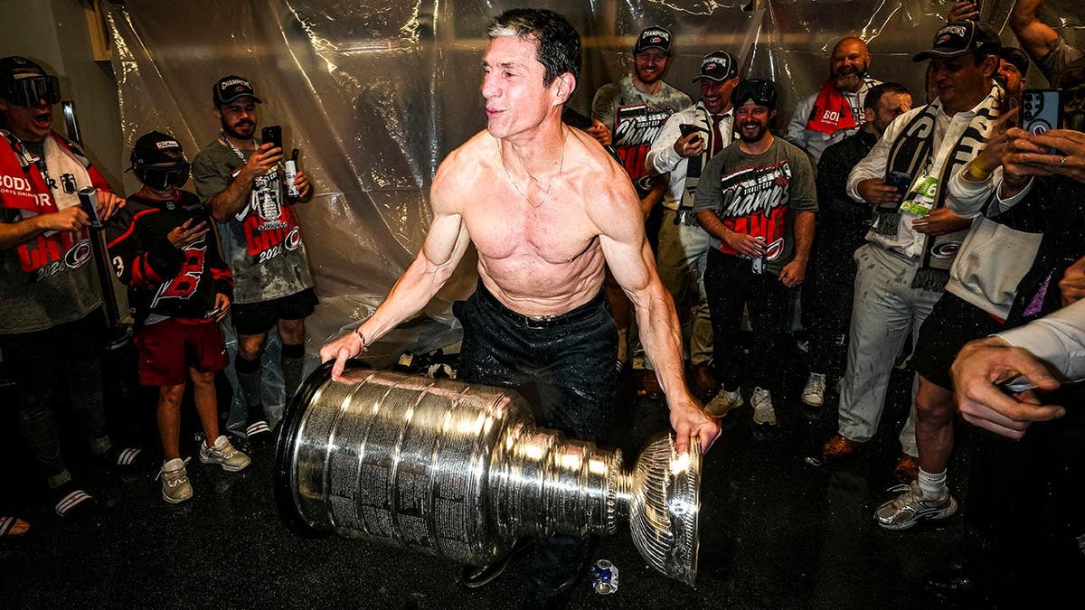 Rod Brind'Amour raises the Stanley Cup in a locker room after winning the game.