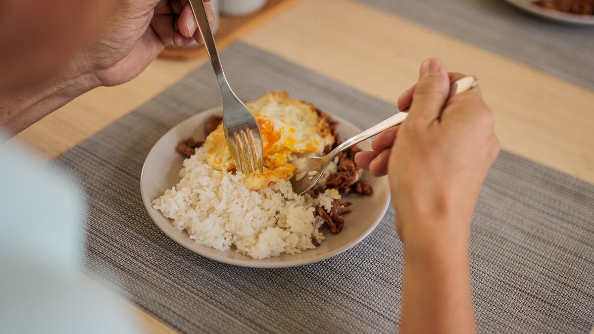 Senior Thai man eats rice, eggs, and meat at a dining table.