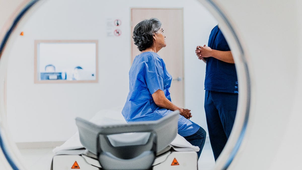 Senior woman talks to a nurse during an MRI scan at a hospital.