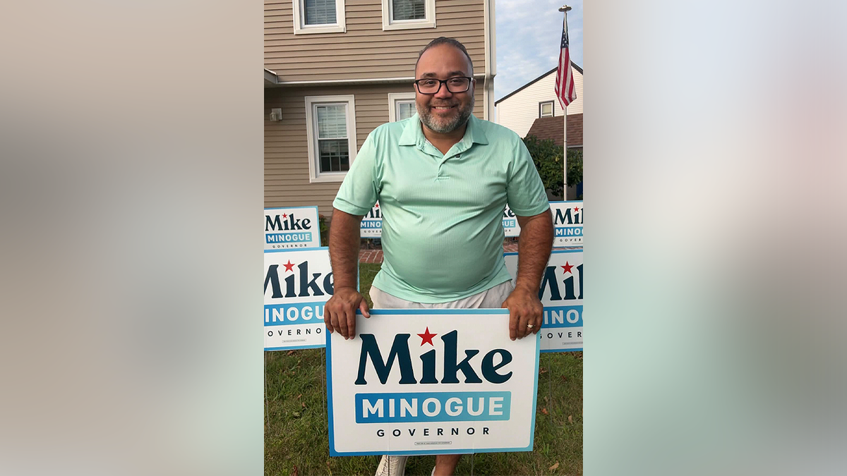 Shawn Oliver holds a Mike Minogue for governor sign outside a home