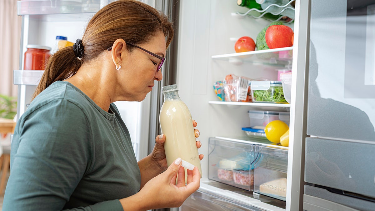 Disgusted woman smelling expired milk by the fridge