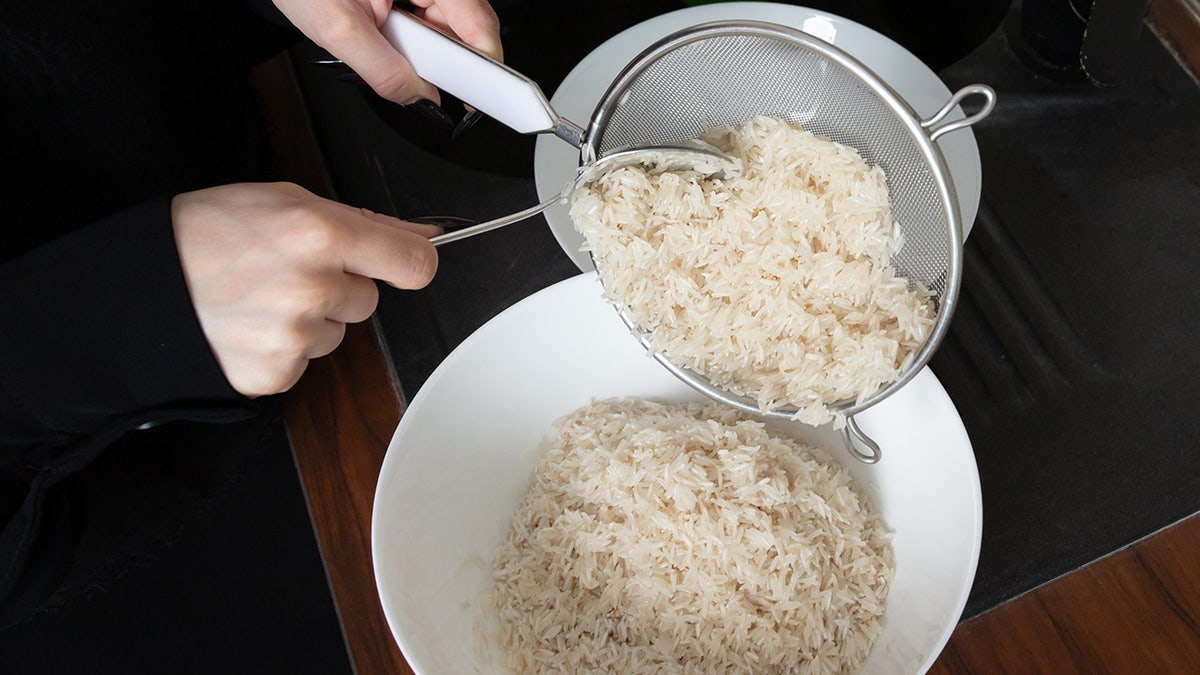 closeup of hands draining soaked long grain rice through a metal sieve into a bowl, showing an important preparation step for homemade festive poultry and rice dishes