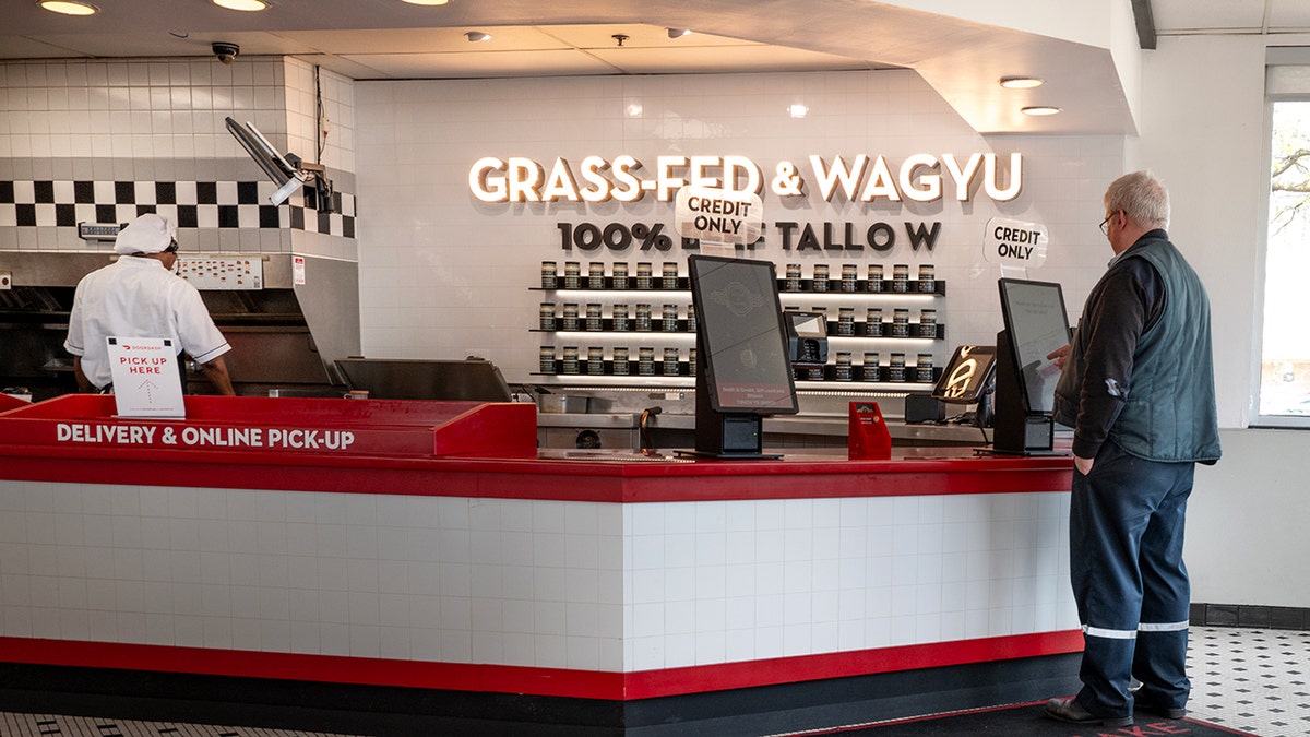 A customer orders from a Steak 'n Shake near a sign that says "Grass-Fed & Wagyu."